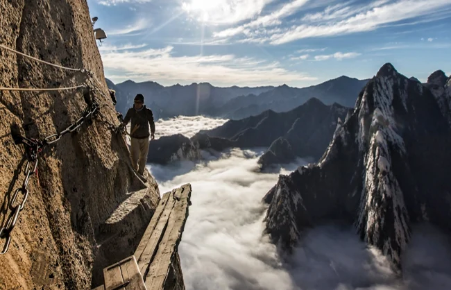 Tourists safely strapped into harnesses navigating the steep wooden Mount Huashan plank walk
