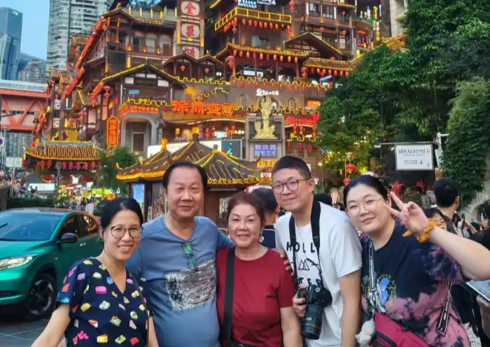 Hongya Cave Chongqing Tour | China Xian Tour: Private & Tailor-Made China Tours Five people smiling for a group photo in front of a brightly lit traditional Chinese temple with red lanterns and pagoda-style roofs.