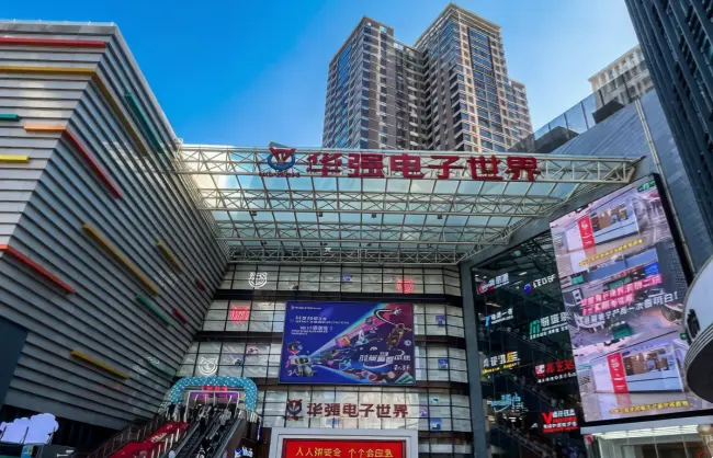 shenzhen-huaqiangbei-electronics-market | China Xian Tour: Private & Tailor-Made China Tours Exterior of a modern electronics market with a glass canopy and a red Chinese sign reading 'åå¼ŗēµåäøē' above the entrance in a busy urban plaza.