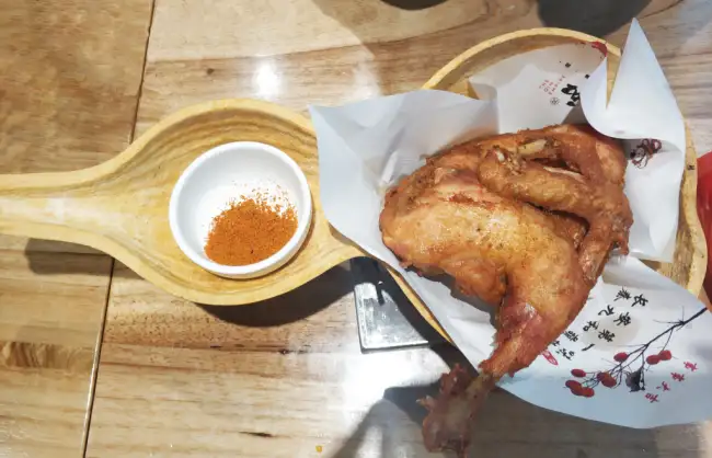 hulu chicken | China Xian Tour: Private & Tailor-Made China Tours Fried chicken wings on a wooden serving tray with a small white bowl of orange seasoning.