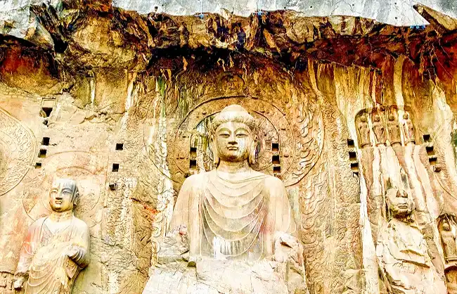 Rock-carved Buddhist statues in a cave temple, with a central large Buddha and two smaller figures beside it