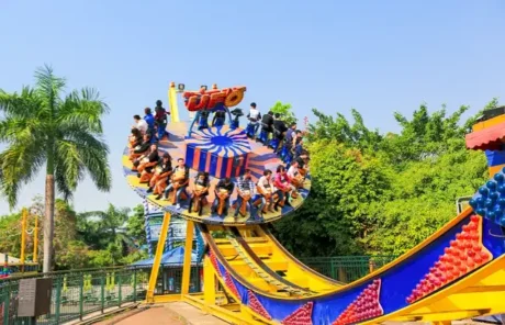 shenzhen happy valley | China Xian Tour: Private & Tailor-Made China Tours People seated on a circular rotating amusement ride at the top platform, surrounded by a bright blue‑and‑yellow track at a sunny park with palm trees nearby.