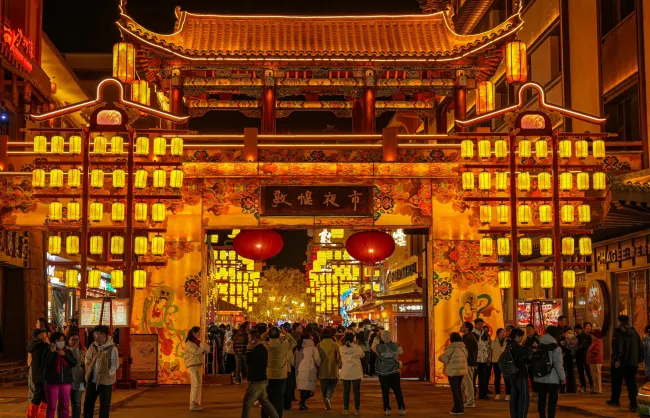dunhuang shazhou night market | China Xian Tour: Private & Tailor-Made China Tours Colorful Chinese temple gate at night, illuminated by yellow lanterns, with a crowd entering through an ornate archway accented by red lanterns.