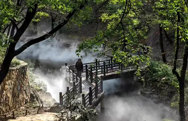 flower creek | China Xian Tour: Private & Tailor-Made China Tours Wooden boardwalk through a misty forest beside a steaming pool; a person stands on the railing.
