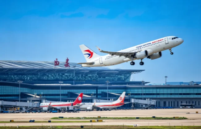 xian-xianyang-international-airport | China Xian Tour: Private & Tailor-Made China Tours White passenger jet lifting off from a runway beside a glass-airport terminal, with two red-tail planes on the tarmac.
