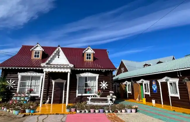 Colorful wooden cottages with red and green metal roofs, white trim, and potted plants along a bright path in front of them.